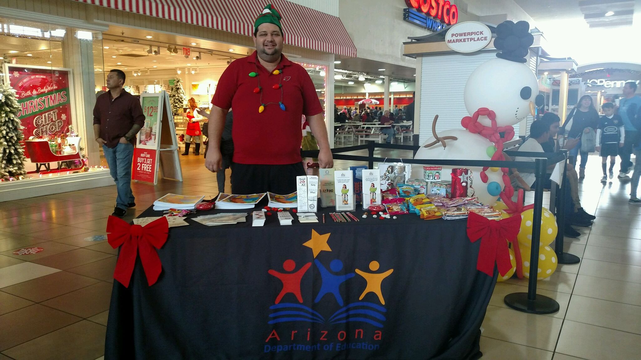 Man in red wearing elf hat stands in front of table with educational materials.