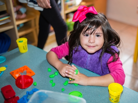 Photo of girl with a pink bow playing with play-doh