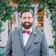 A man with dark hair and a dark beard wearing a suit with a bow tie